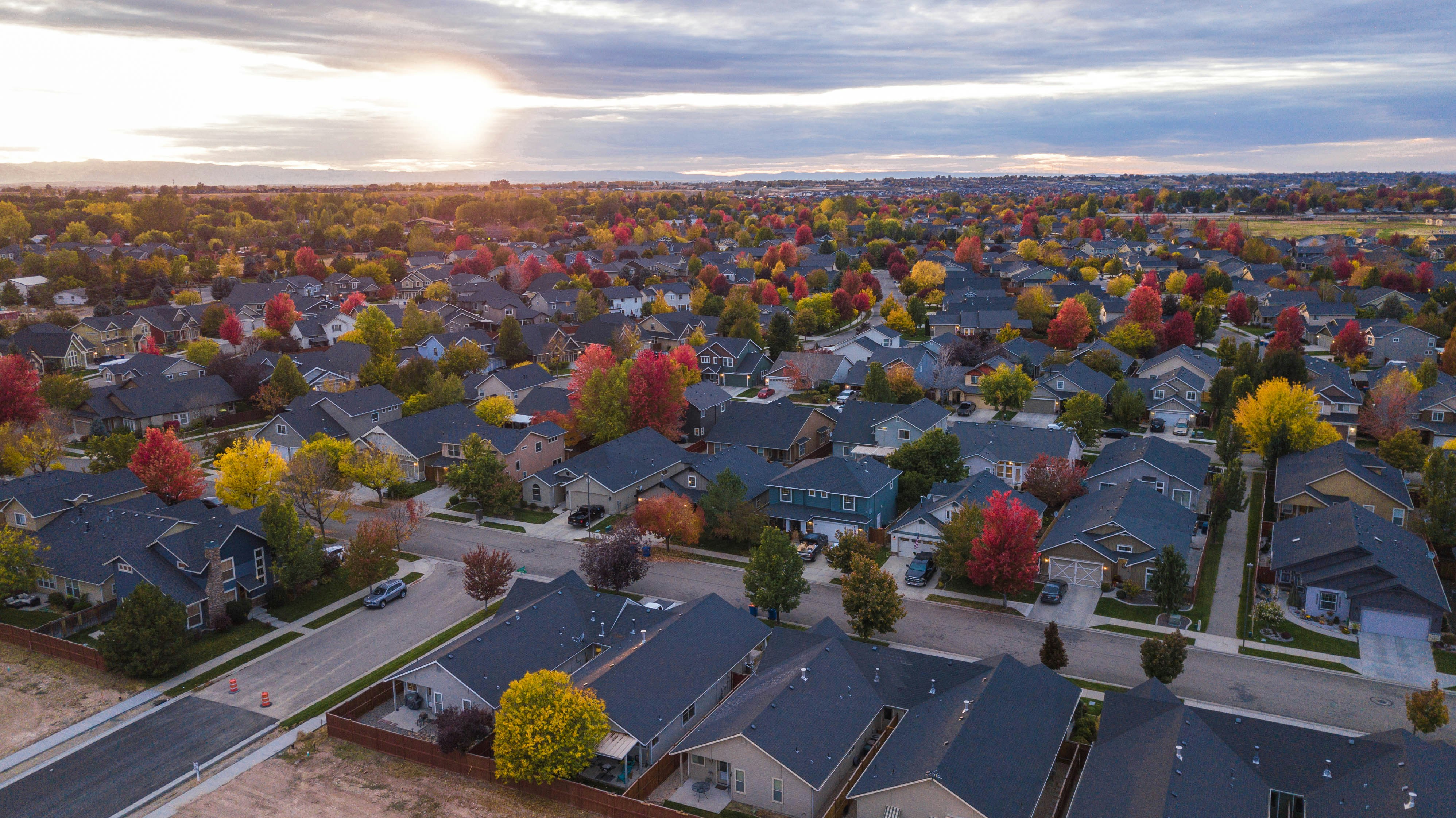 aerial view of a surburban neighborhood at sunset, with rows of houses and trees lining in between.