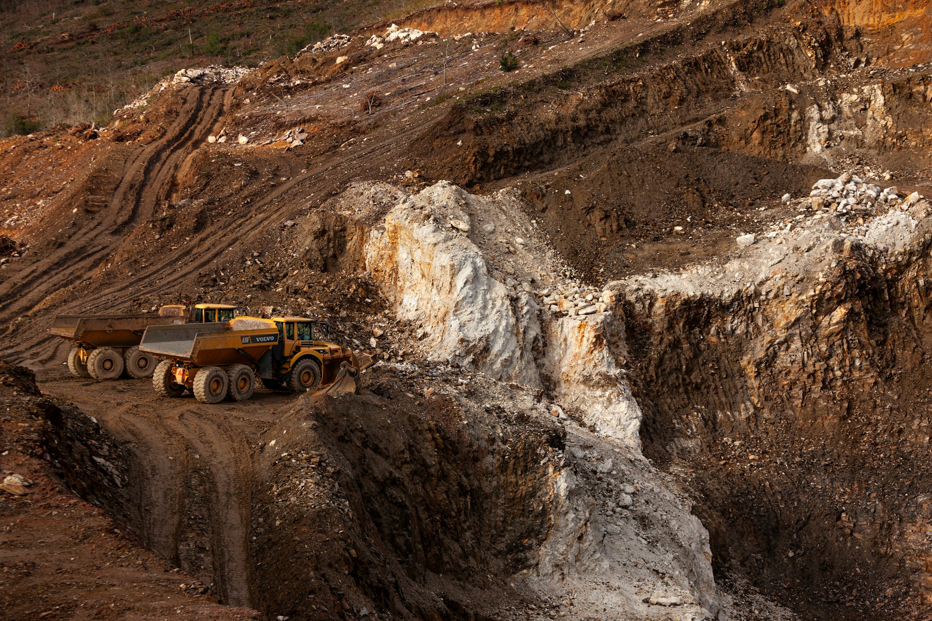 two large trucks parked in an open pit quarry exploited for lithium and other raw materials